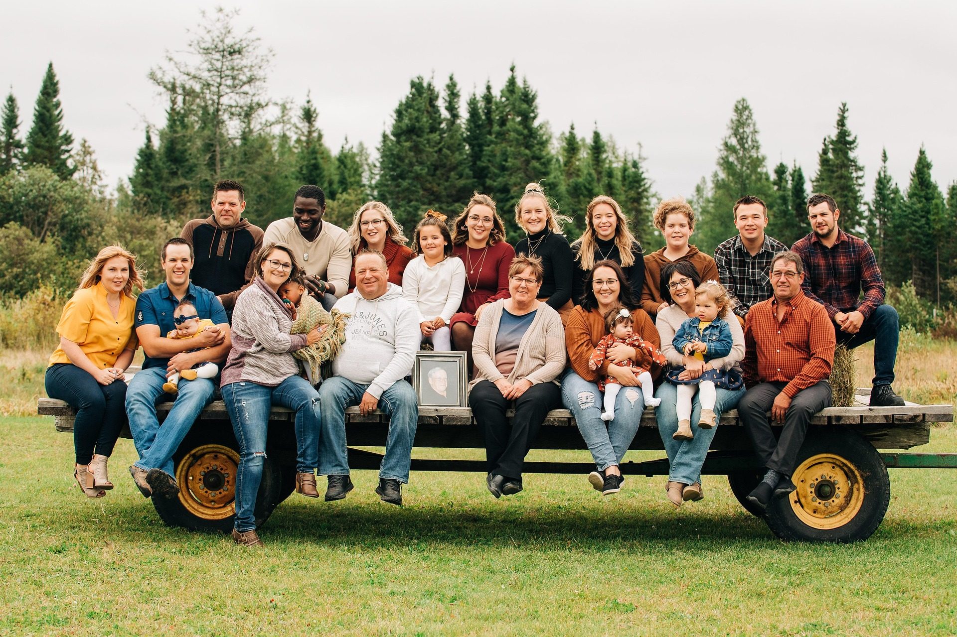 A multigenerational group gathered on a wagon outdoors, with a framed portrait at the center.